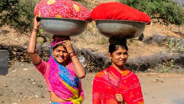 Zwei Frauen auf dem Weg zum Fluss, um die Kleider zu waschen. Gesehen in Kumbhalgarh, Rajasthan, Indien.